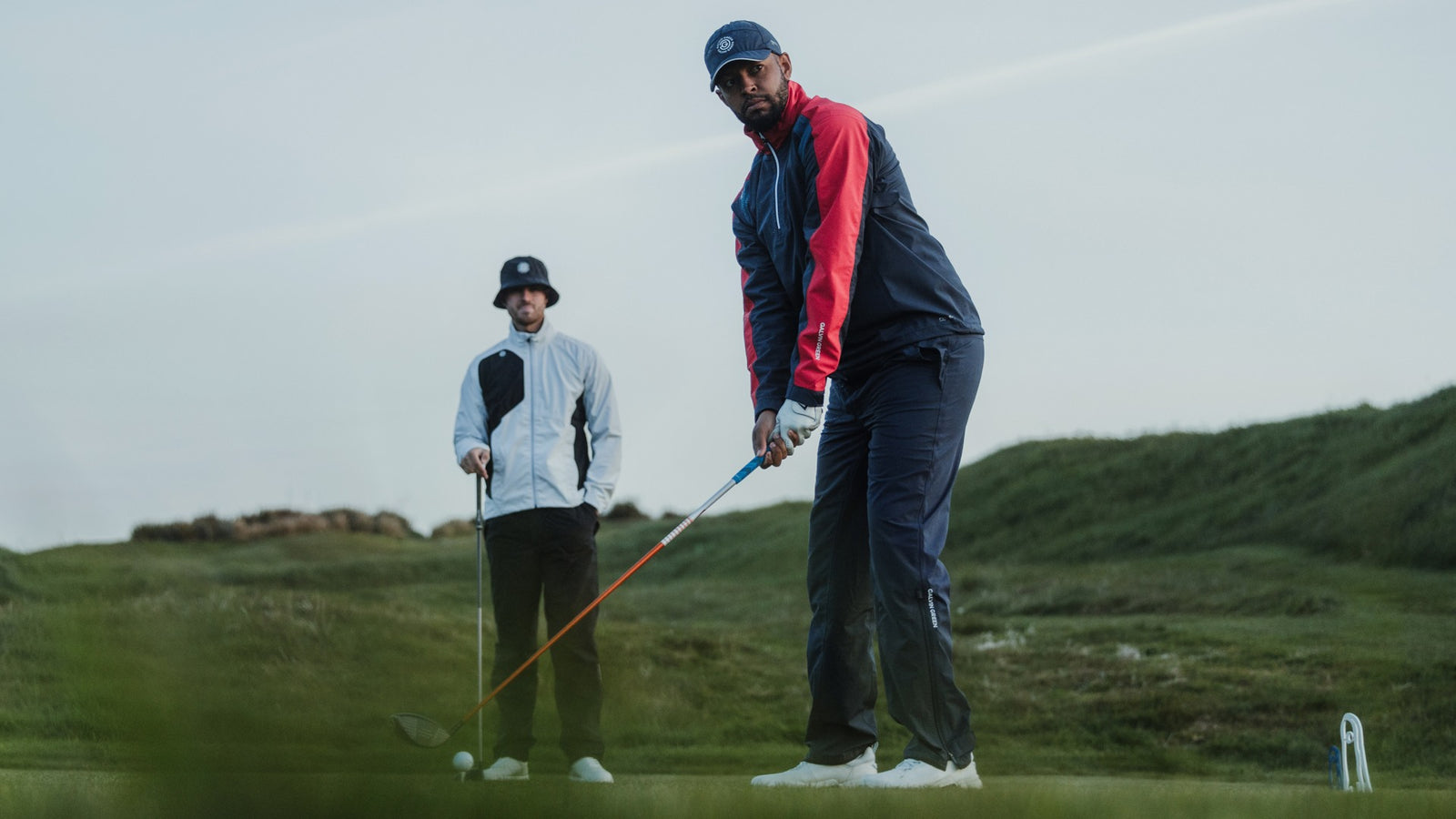 Two male golfers on tee, wearing golf rain clothes