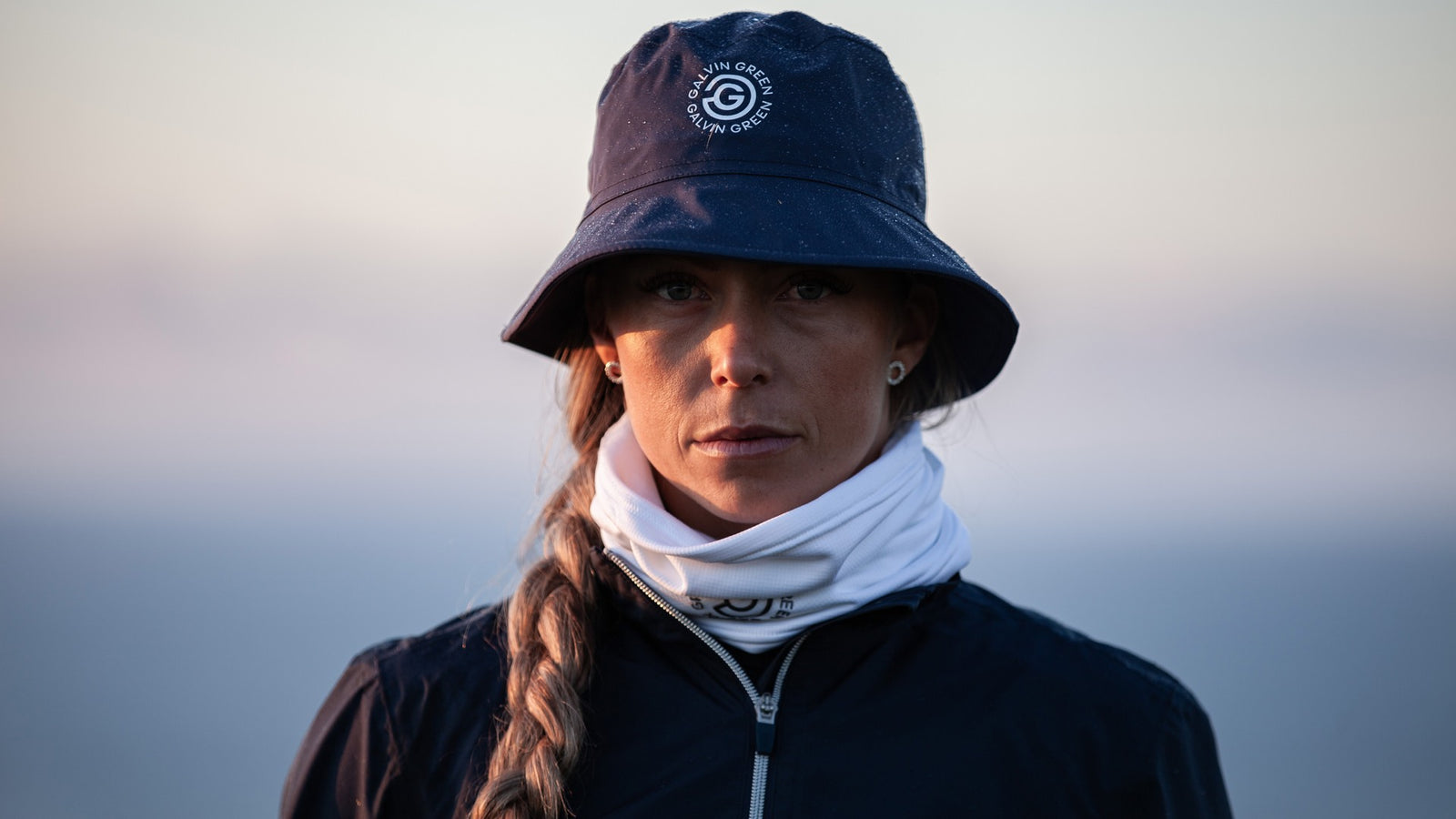 A female golfer wearing a navy rain hat a white snood and a navy rain jacket.