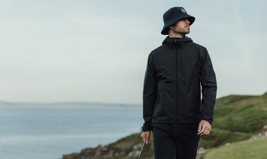 Male golfer wearing a black hat and a black rain jacket