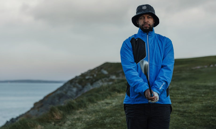 Male golfer holding his club, wearing a golf rain hat and a blue rain jacket