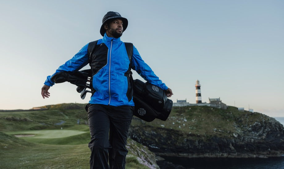 male golfer carrying his bag wearing a blue golf rain jacket