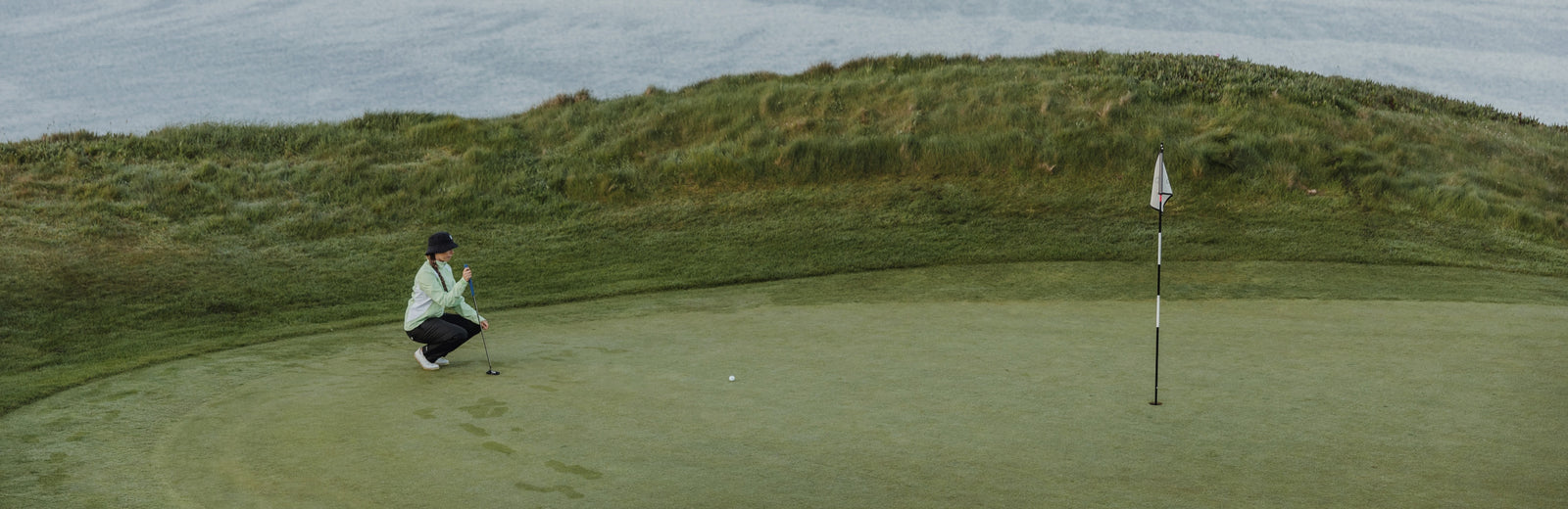 a female golfer reading putting line, wearing green and black rain golf gear