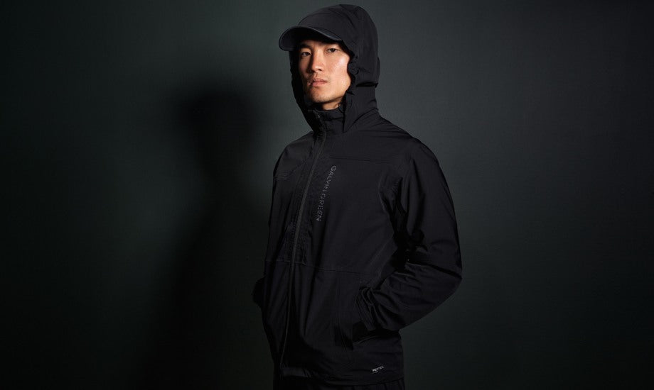 A male wearing a black golf rain jacket with a hood