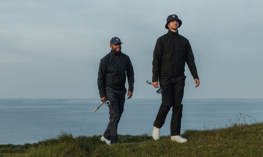 two male golfers walking on a golf course wearing golf rain gear