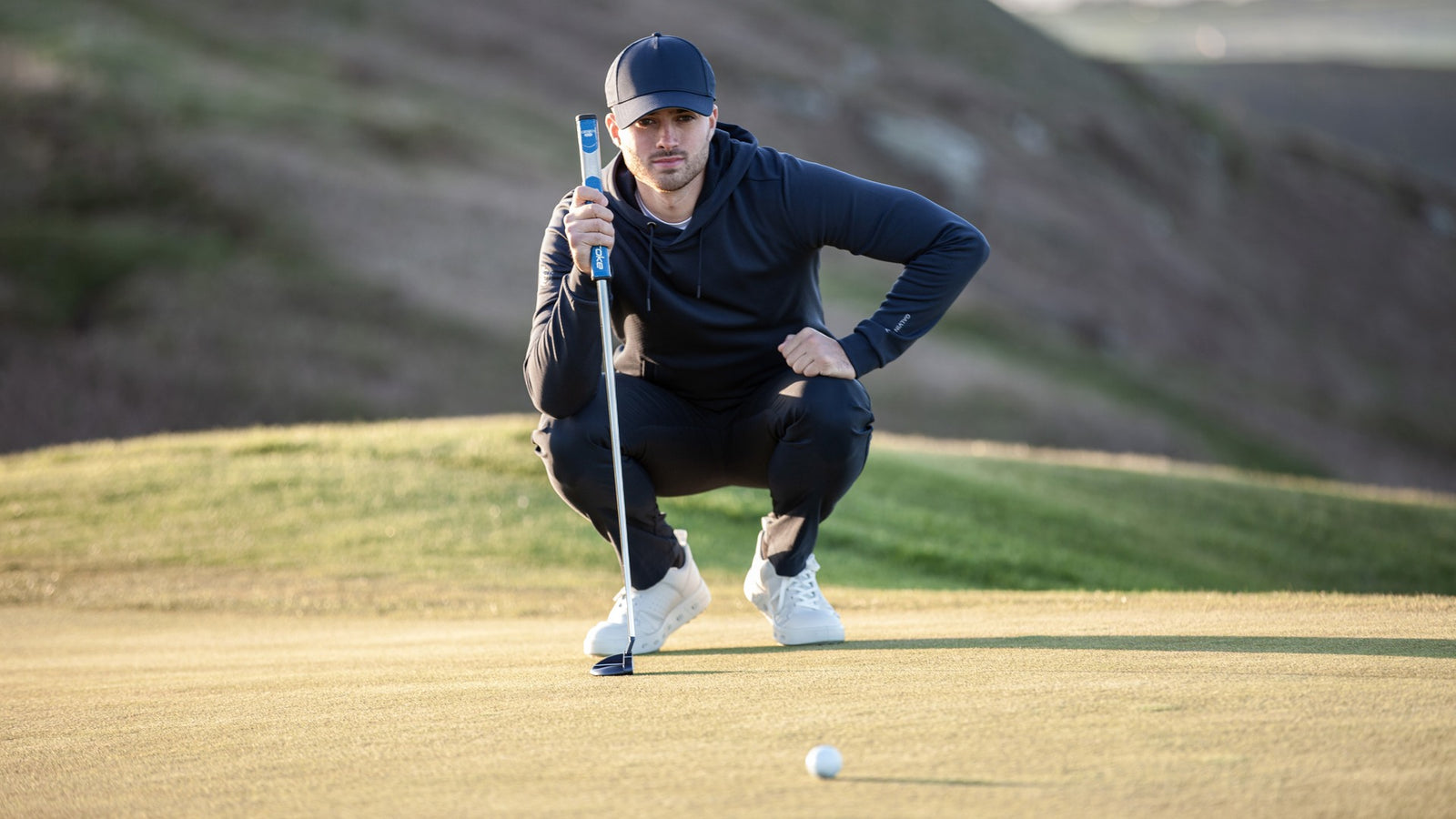 A male golfer holding his putter and reading his putting line 