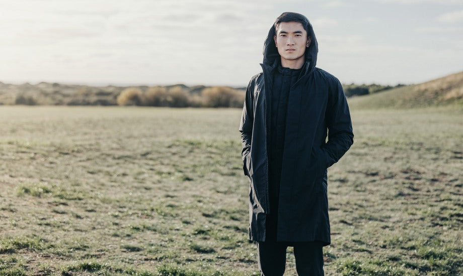 A male standing on a open field wearing a black jacket with a hood