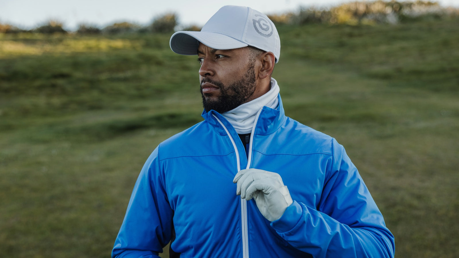 male golfer wearing a blue windbreaker jacket and a whit cap