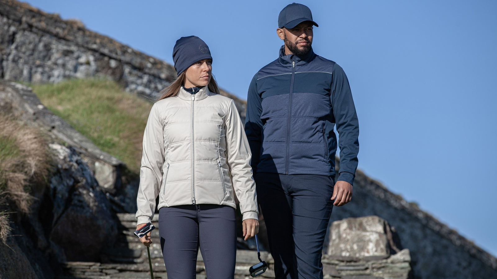 A male and female golfer walking with their putters in their hands.