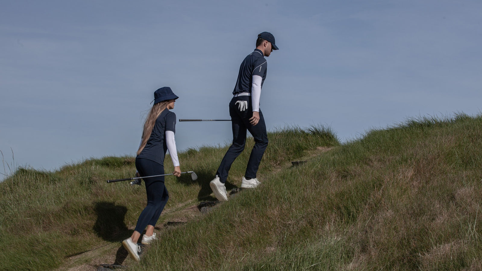 Male and female golfer carrying their golf club walking up a hill