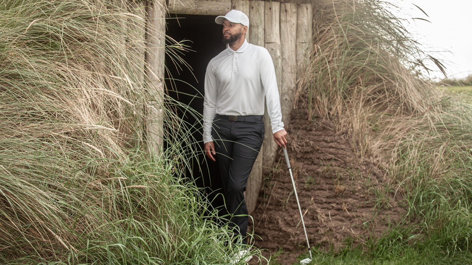 A male golfer with a golf club wearing navy golf pants and a whit lon sleeved polo shirt