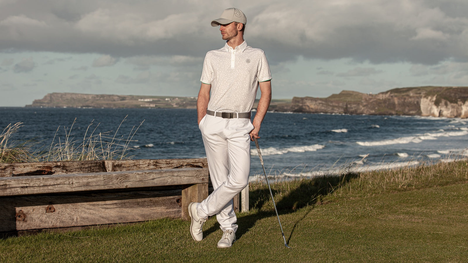 A male golfer holding his golf club standing in front of the sea