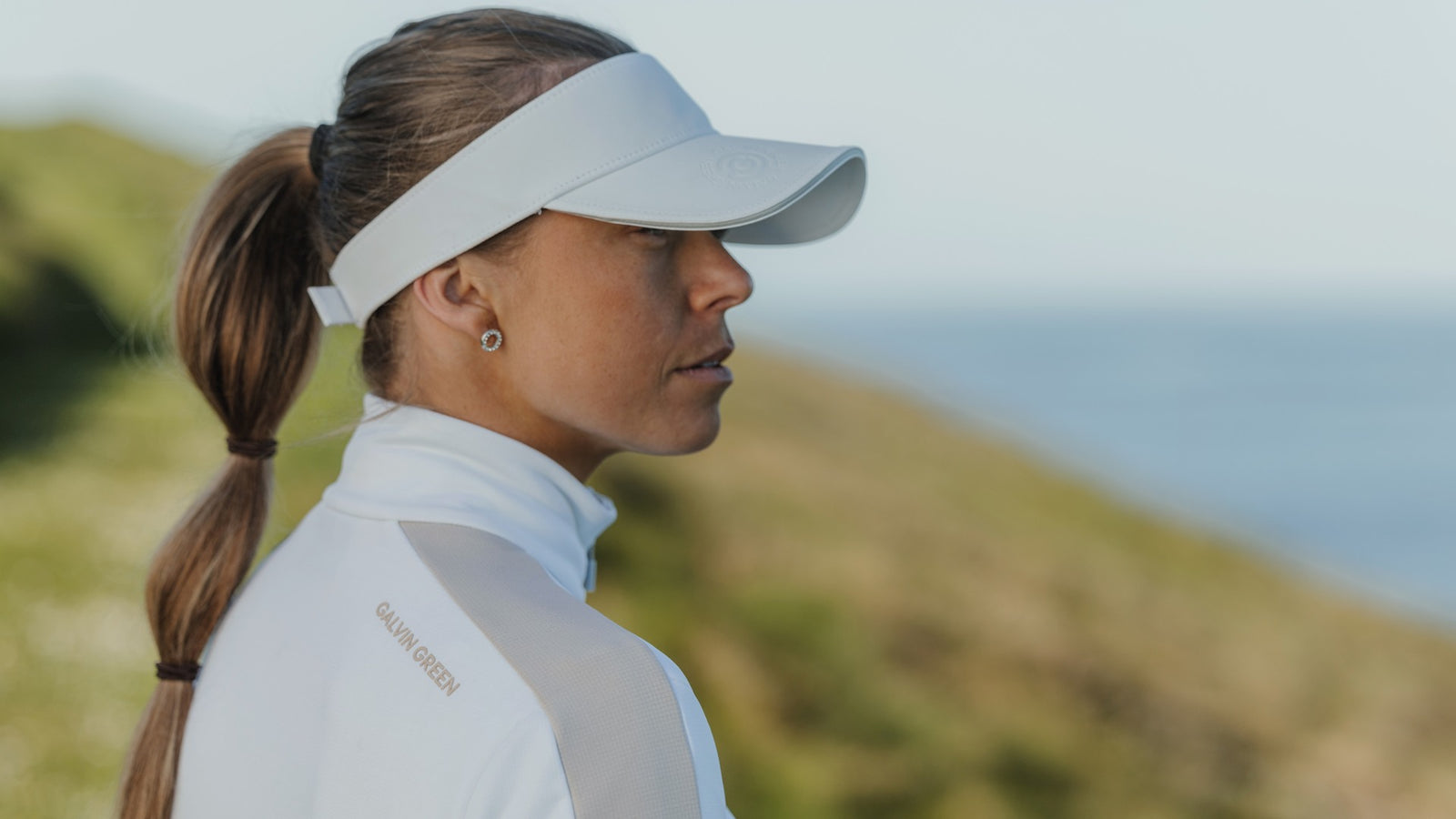 A female golfer wearing a white golf visor and a white mid layer sweater.